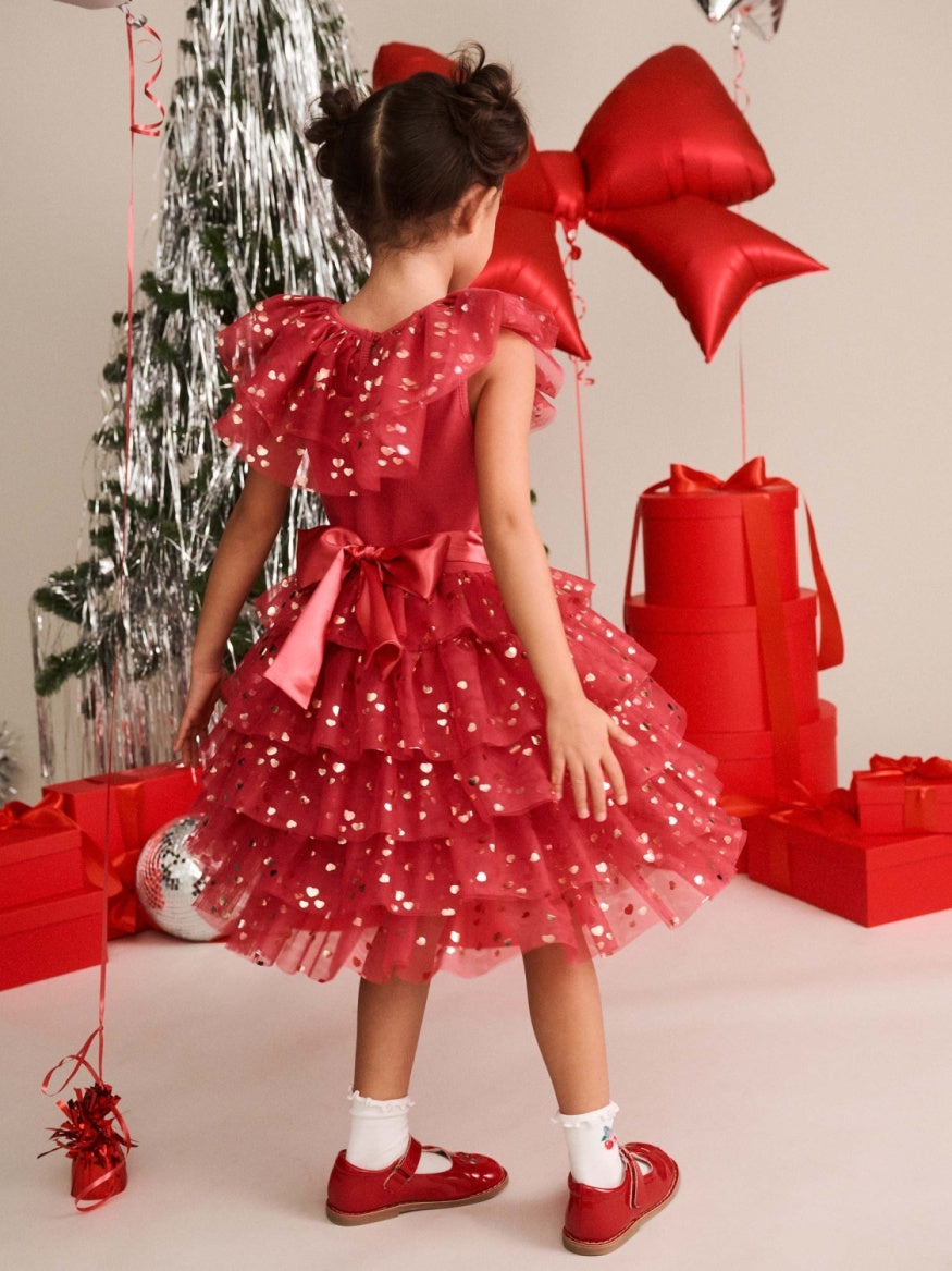 Girl wearing Huxbaby festive heart bow tiered tulle dress featuring a soft tulle skirt, layered tiers, heart detailing, and a decorative bow for a whimsical children’s occasion outfit.