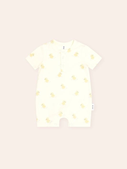 Cream short-sleeve baby Henley bodysuit with an all-over yellow rubber duck print. Features a three-button Henley neckline, soft cotton fabric, and snap closures at the crotch for easy nappy changes. Lightweight and perfect for everyday wear in warmer weather.