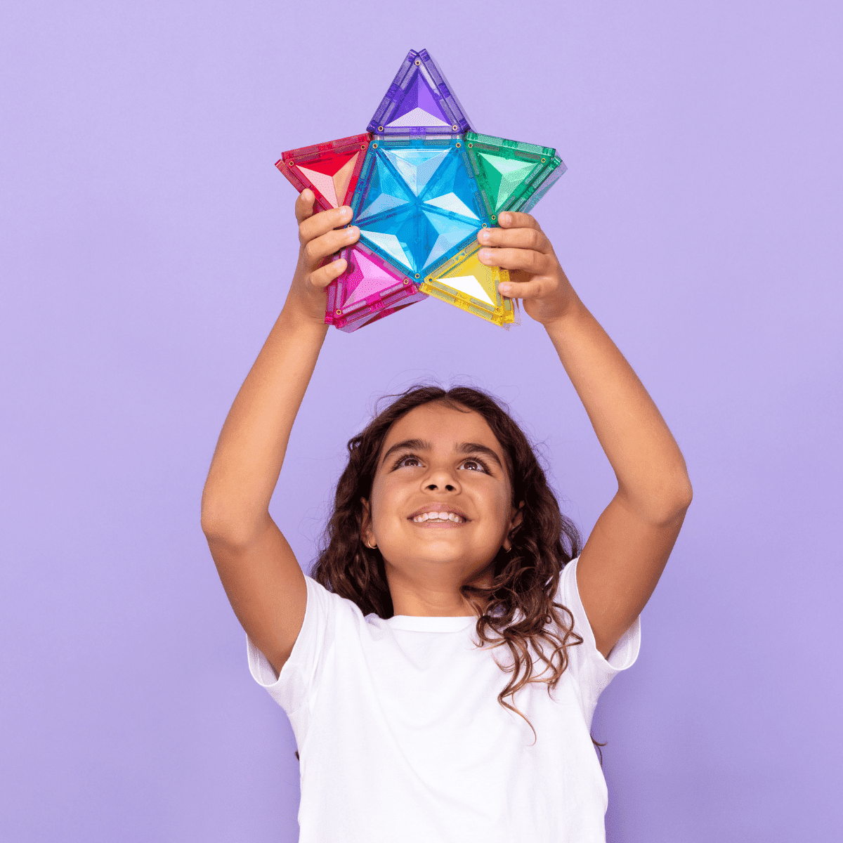 Two children building a tall tower from colourful magnetic tiles on a living-room floor