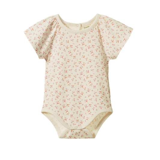 Nature Baby Faye Bodysuit in Dandelion Print, featuring a soft cream organic cotton bodysuit with an all-over yellow dandelion floral pattern. The long-sleeve design has a gathered empire waist, gently flared silhouette, envelope neckline, and snap closures at the crotch for easy dressing.