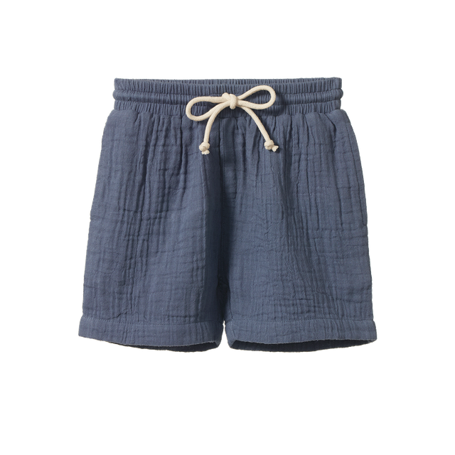 Nature Baby James Shorts in Muslin Vintage Indigo, featuring lightweight muslin shorts in a soft vintage indigo blue colour. The relaxed-fit shorts have an elastic waistband with adjustable drawstring, side pockets, and a comfortable everyday design for children.